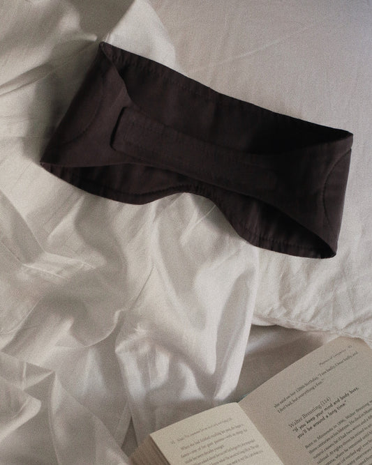 Cosy London eye mask on a bed beside a book 