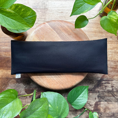black weighted eye pillow with green leaves surrounding it 
